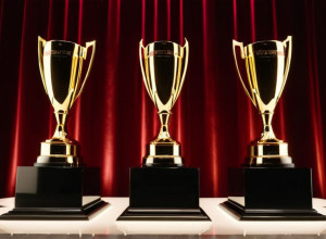 Элегантная церемония награждения: сцена с мерцающими огнями, абстрактные трофеи на пьедесталах, праздничная атмосфера в роскошном бальном зале отеля. Кинематографическое освещение, 8k, гиперреалистично.